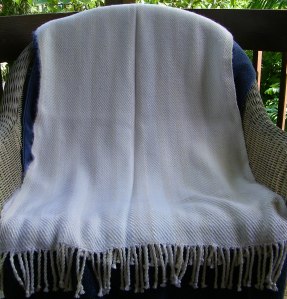 Shawl draped vertically over a chair back and seat, with twisted fringe hanging over the chair edge at the bottom.