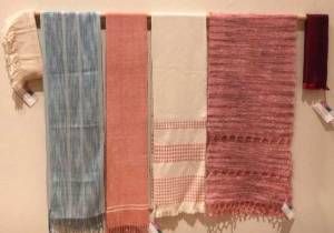 row of scarves hanging, with blue ika on left, then Rosy Dawn, then white with pink dice weave, and then a pink mohair one on the right. At the ends are two small pieces fashioned into collars